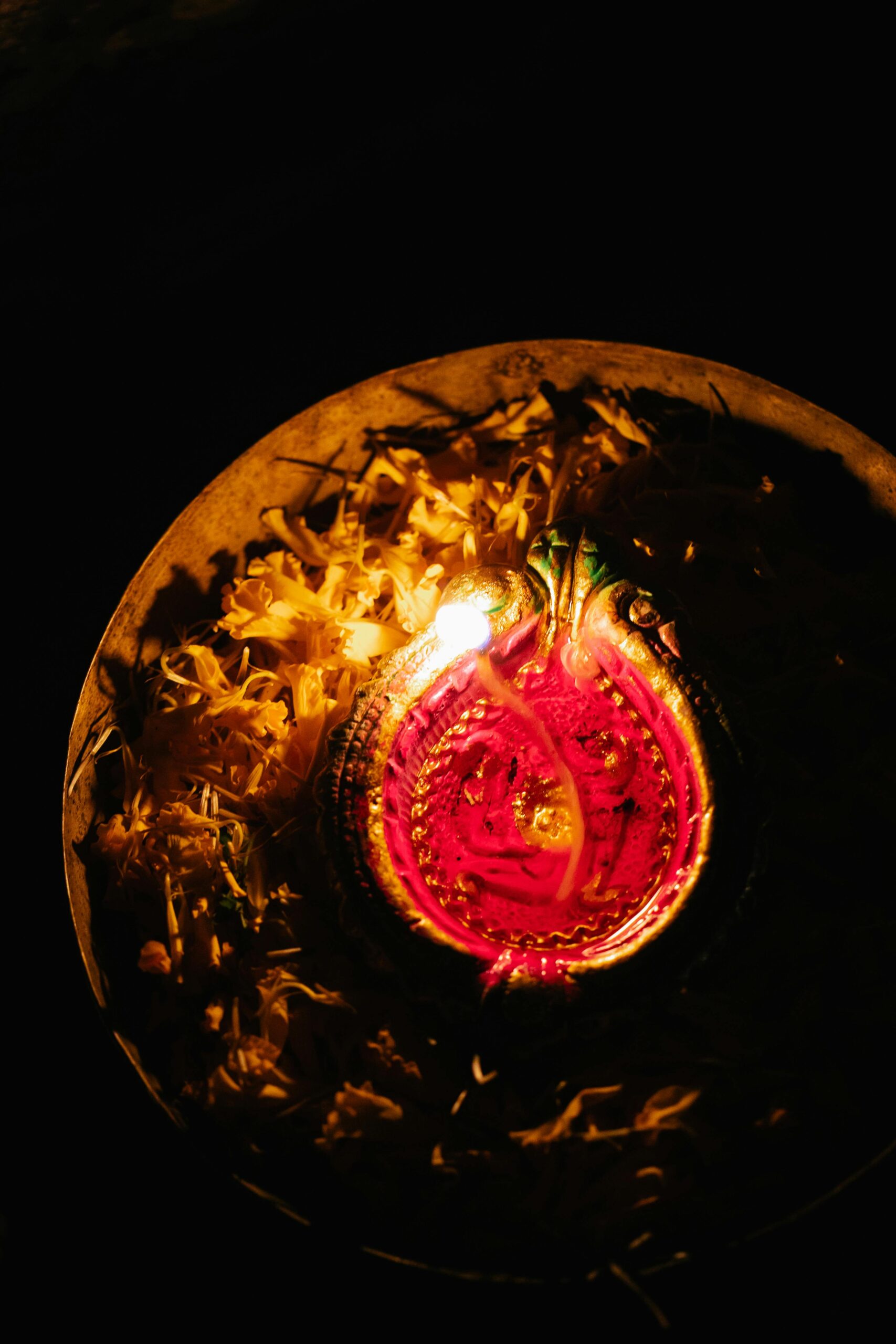 A vibrant diya placed within floral petals, shining brightly in the dark, evokes a warm, festive ambiance.