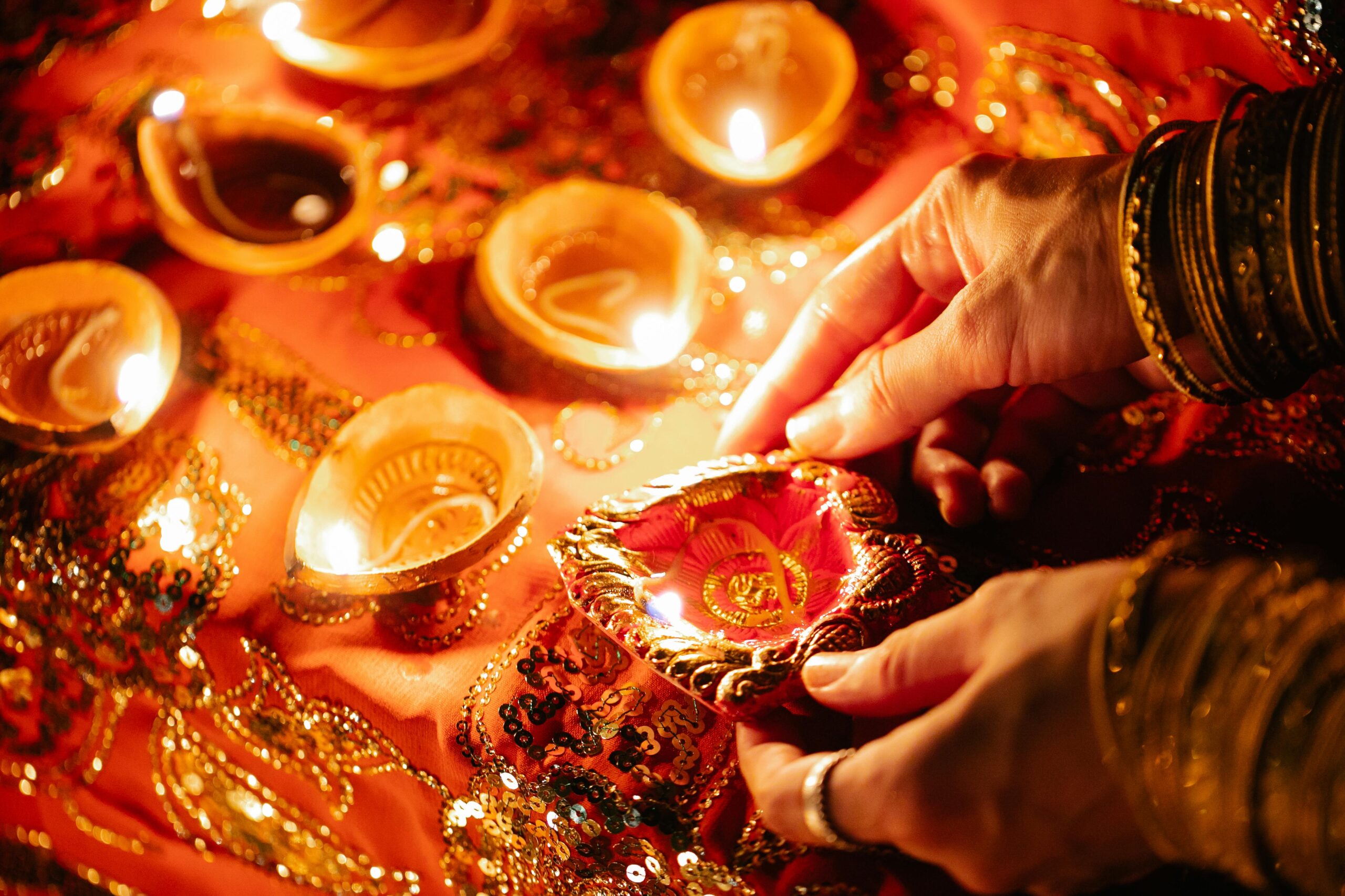 Close-up of hands lighting decorative oil lamps for Diwali celebration, creating a warm festive ambiance.